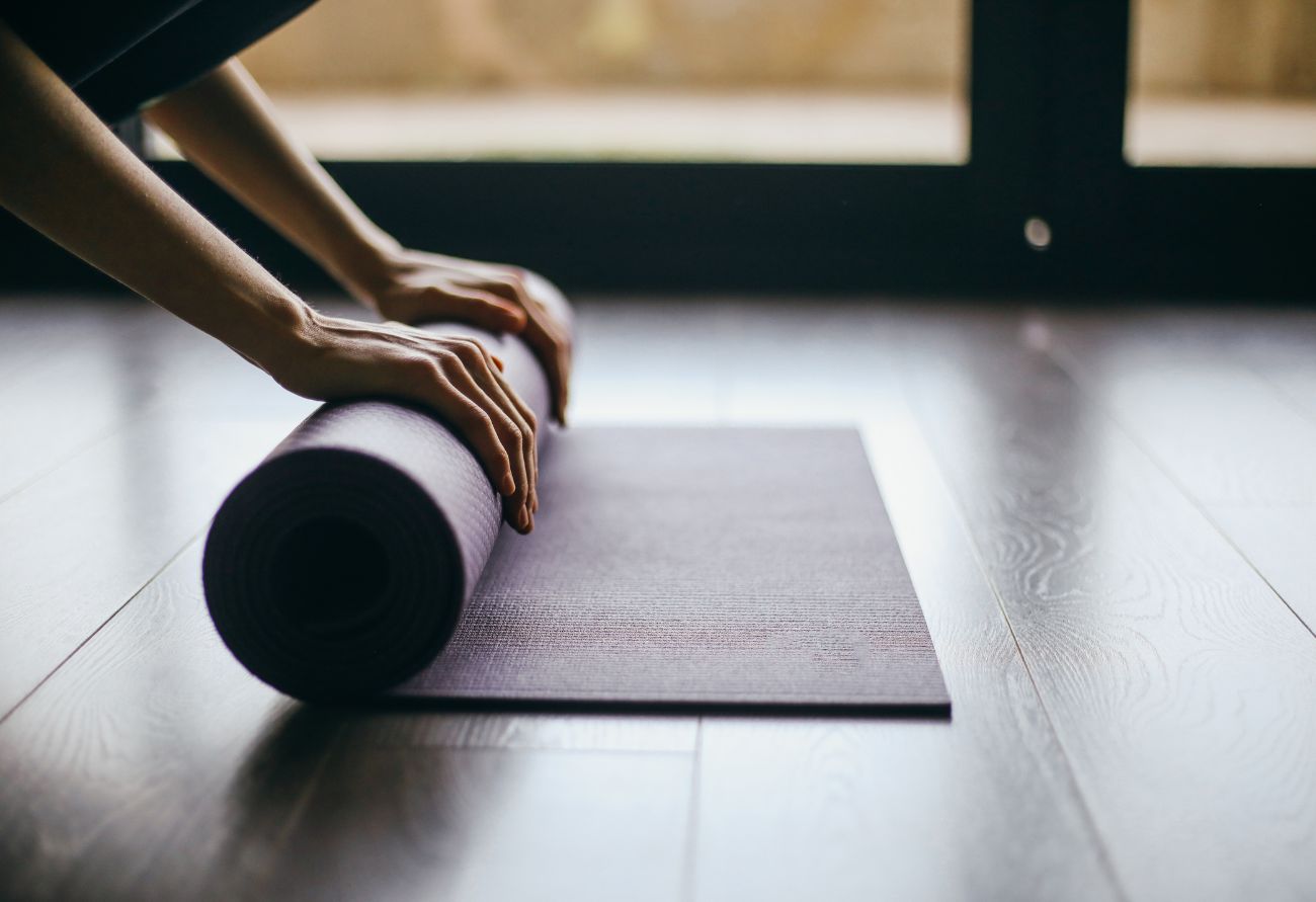 En person rullar ihop en yogamatta för att träna i det nya normala
